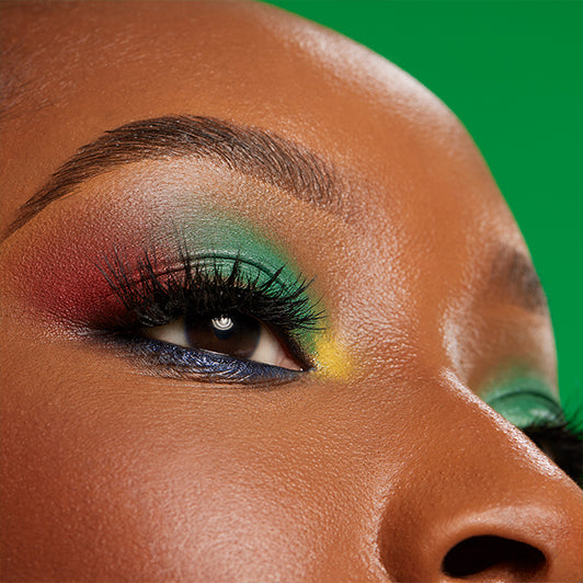 Close-up of an eye with a vibrant multi-color look using red, green, yellow, and blue eyeshadows from the Black Radiance x Cross Colours palette.