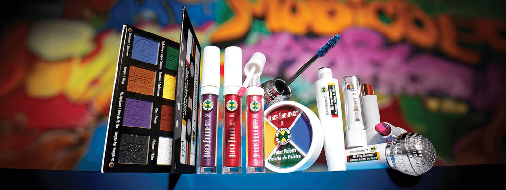 Colorful Black Radiance x Cross Colours makeup collection including eyeshadow palette, lip glosses, mascara, and paint palette, displayed in front of a graffiti-style background.