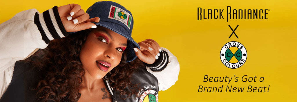 Woman wearing a blue Cross Colours bucket hat and varsity jacket, posing in front of a yellow background for the Black Radiance x Cross Colours beauty collaboration campaign with the tagline “Beauty’s Got a Brand New Beat!”